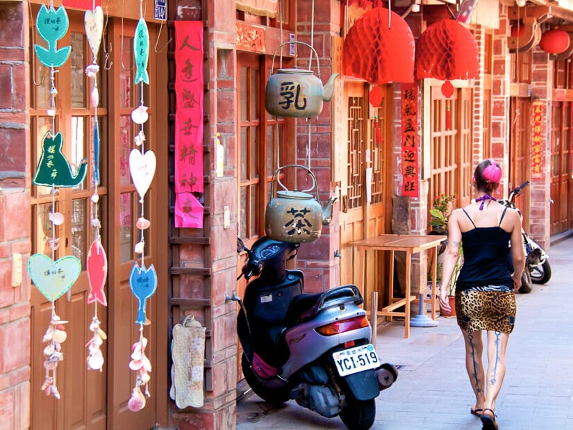 A girl with pink hair walking past traditional wooden houses on Zhongyang Old Street in Magong