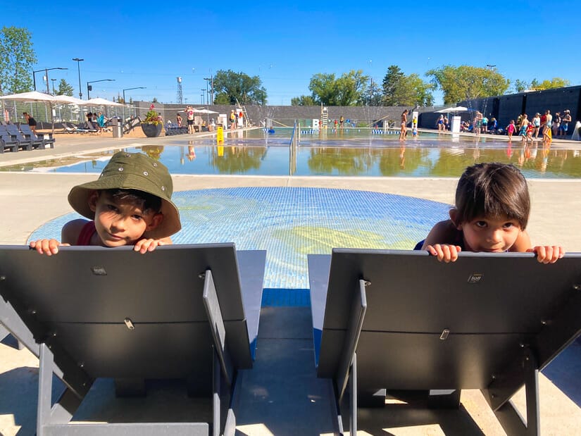 Two kids on beach chairs and Borden Park Natural Swimming Pool in Edmonton