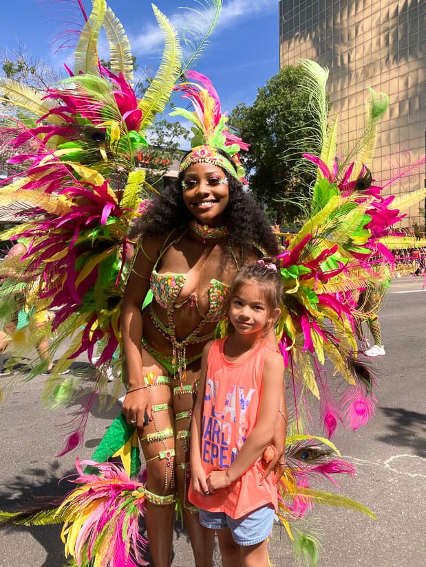 A girl with a Caribbean performer in costume at Edmonton Cariwest Festival