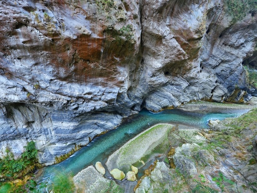 Looking down at a thin, turquoise stream, with towering cliffs opposite