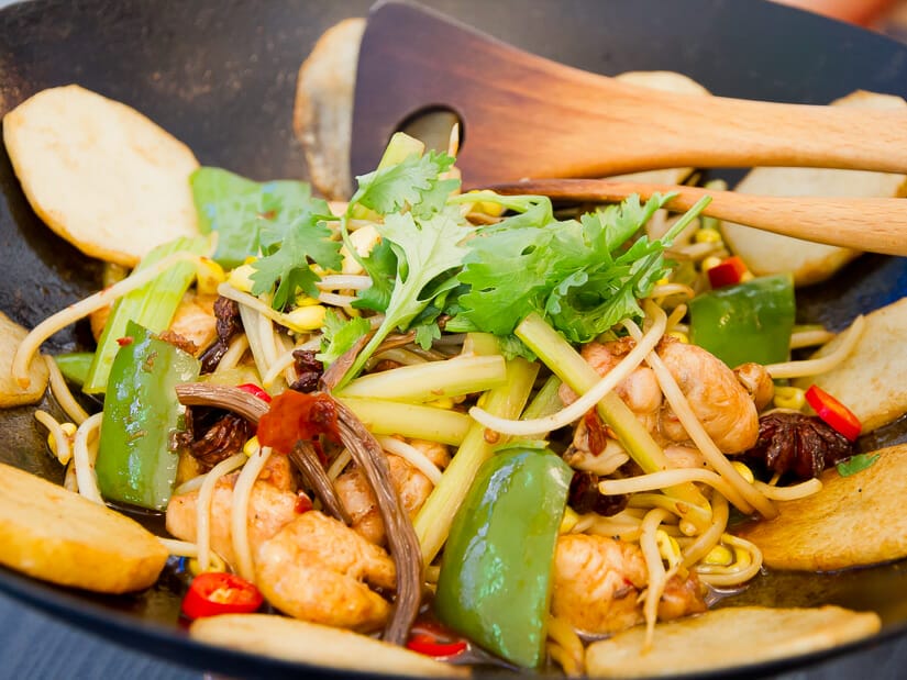 Close up of a stir fry with wooden utensils and round potato slides lining the pot