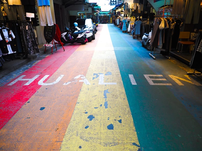 A narrow lane with rainbow stripes painted on the ground and the word Hualien across it in white letters