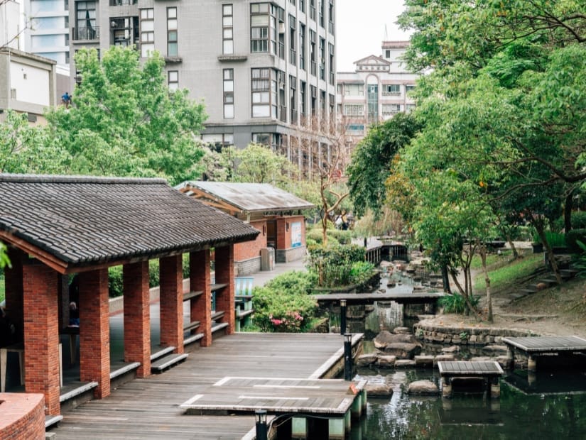 A park with boardwalk and creek and covered hot spring foot soaking tubs on the left