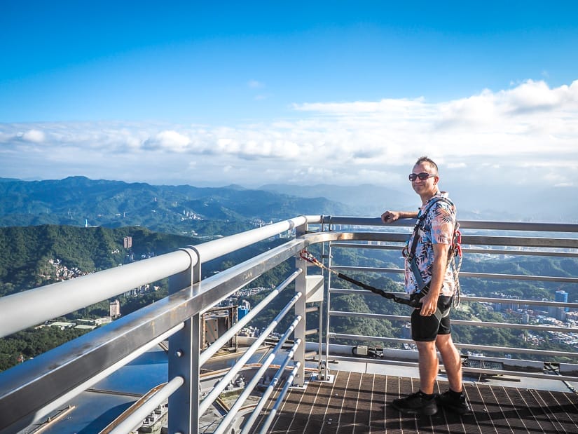Nick Kembel standing on top of Taipei 101 with a cord attaching him to the railing