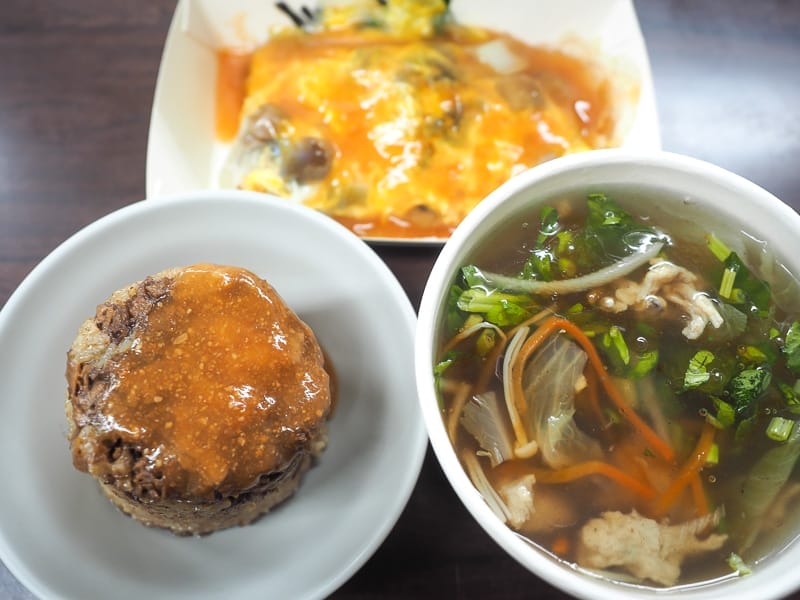 Three vegetarian dishes on a table: a bowl of thick soup, rice tube topped with red sauce, and mushroom omelet