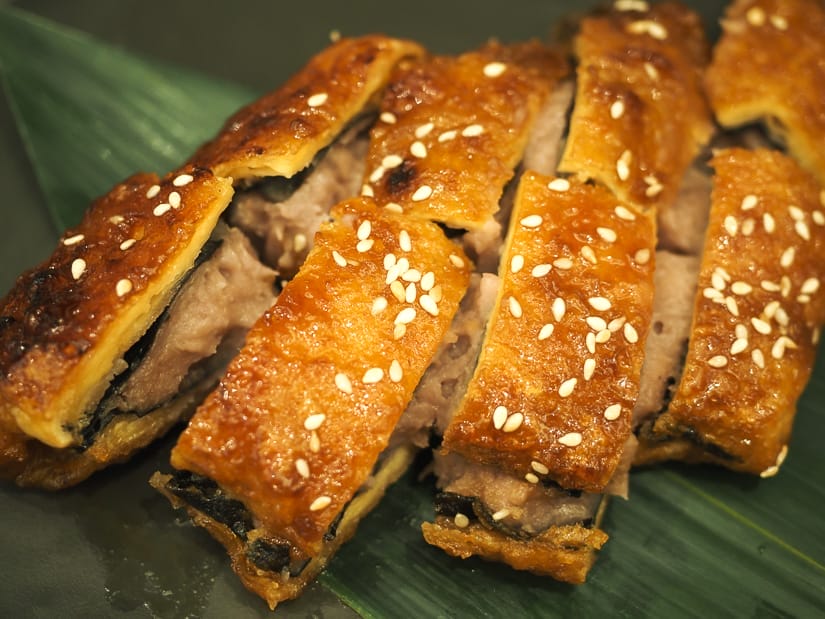A vegetarian dish served on a green leaf, consisting of a patty of fried tofu patty slices into six pieces with taro stuffing inside