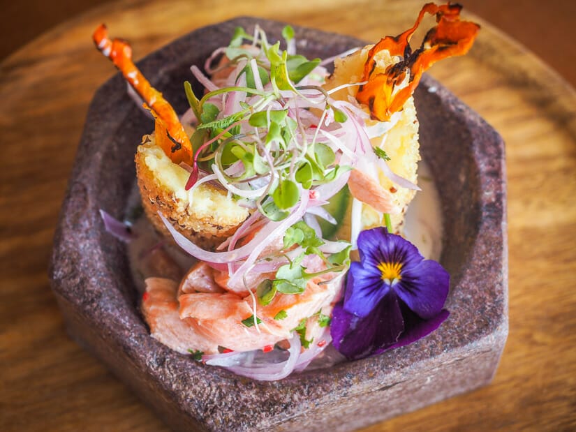 Close up of a fancy dish consisting of ceviche and causas in a stone bowl on a table
