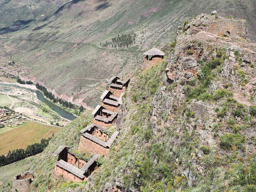A collection of colcas (storehouses) called Hospitainiyoc perched on a cliff, with a river visible in the valley far below behind them