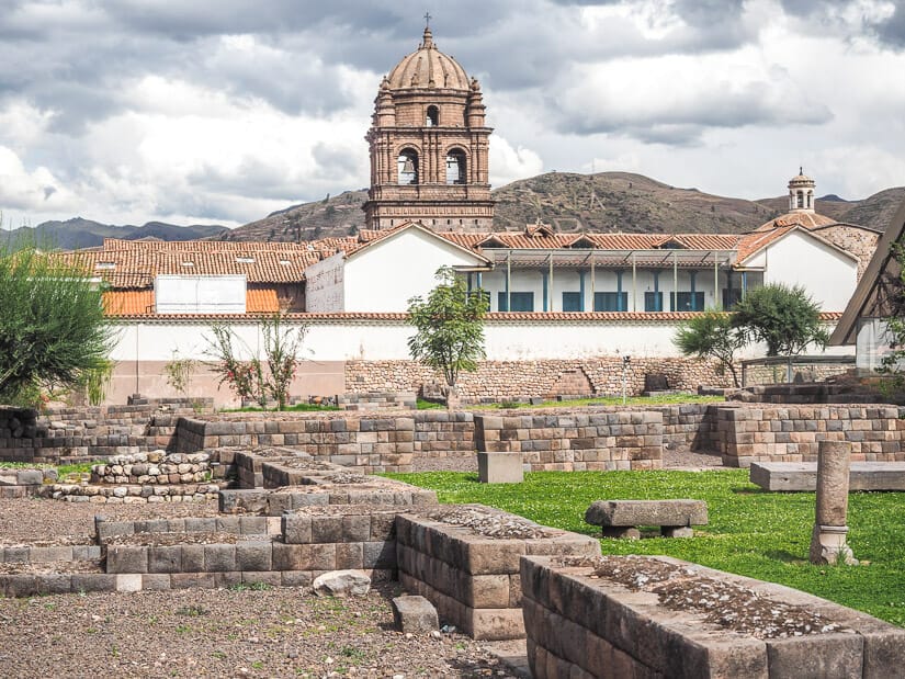 Ruins of Kusicancha in Cusco with a church bell tower in the background