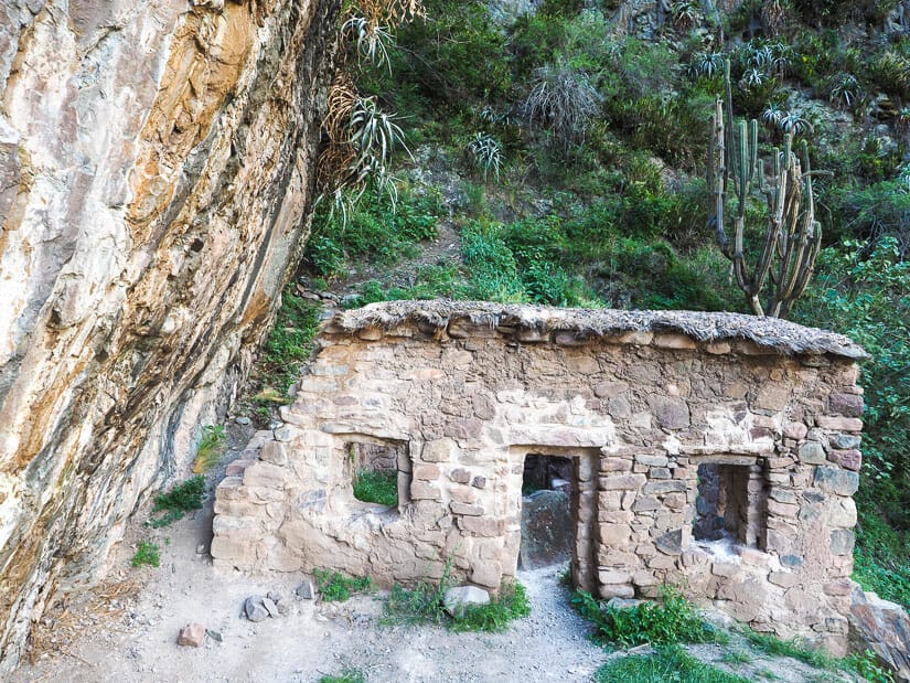 Ruins of a single stone wall with a door and two windows, just beside a cliff face