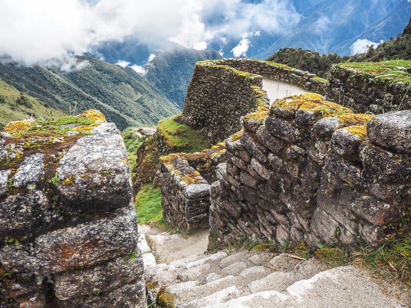 Looking down a staircase at Phuyupatamarca ruins, with mountains and clouds in background