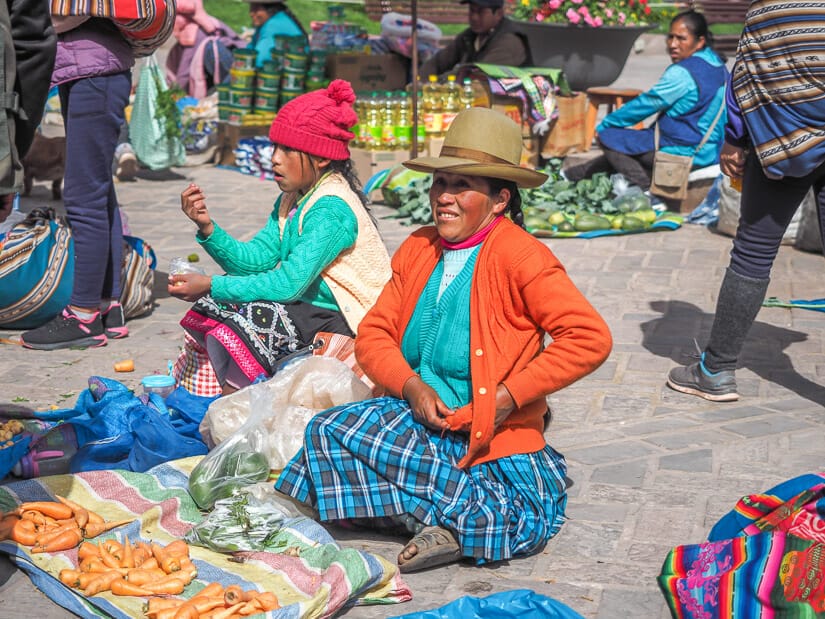 A Quechua woman sitting on the ground selling produce in Pisac Market