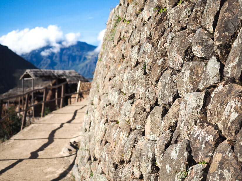 An Incan stone wall with walking path winding around it and mountains visible in the background