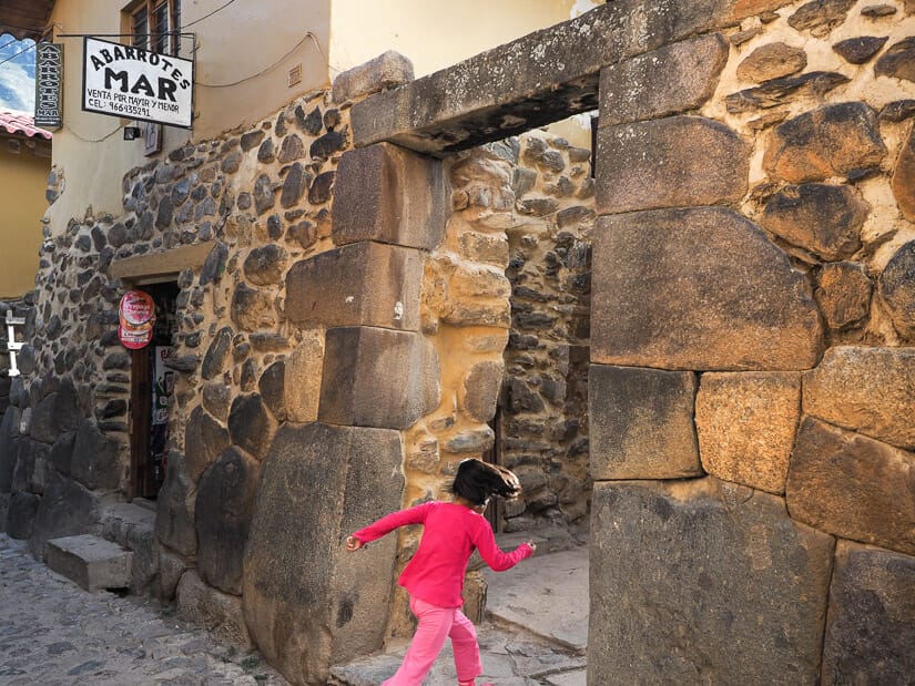 A child wearing pink runs through a stone gate in the Qosqo Ayllu of Ollantaytambo