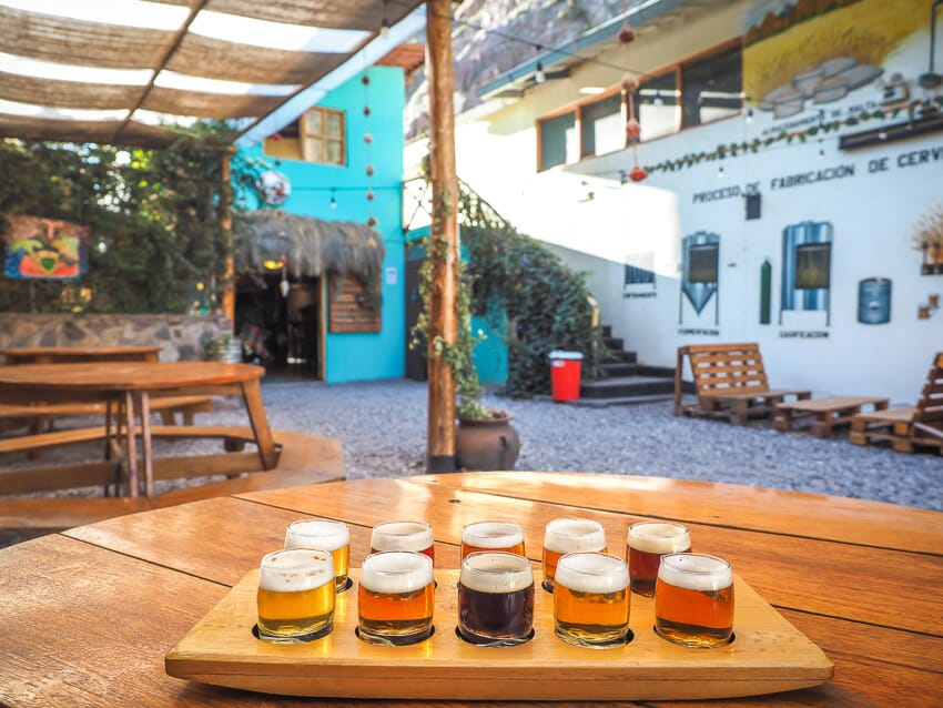A wooden flight of beers with 10 small glasses of beer on a table with a courtyard behind