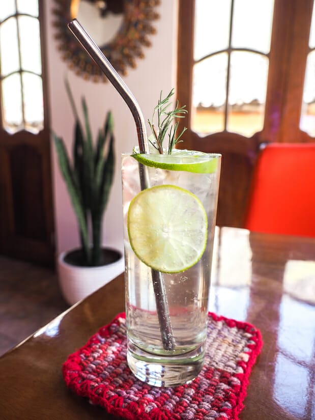 Cocktail in a clear glass with lime slices and rosemary on the table of Amanto restaurant in Ollantaytambo