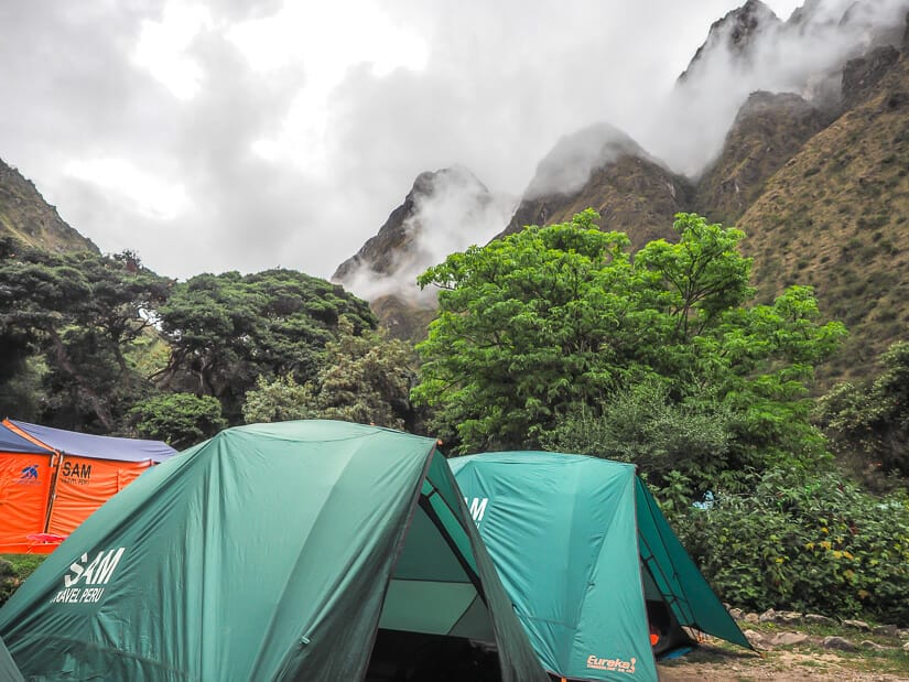 Two green tents and an orange Sam Travel Peru dining tent at Ayapata Camp, with mountain peaks behind