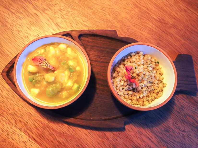 Close up of a bowl of pumpkin stew and a bowl of wheat grain on a wooden, fish-shaped tray