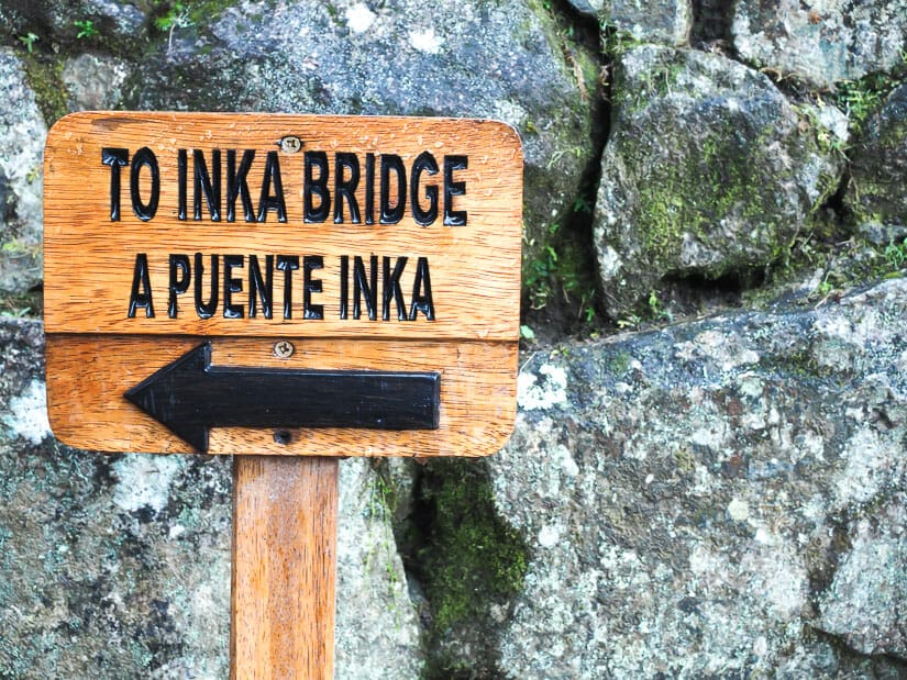 A sign with an arrow and the words "To Inka Bridge, a Puente Inka", with stone Inca wall behind it