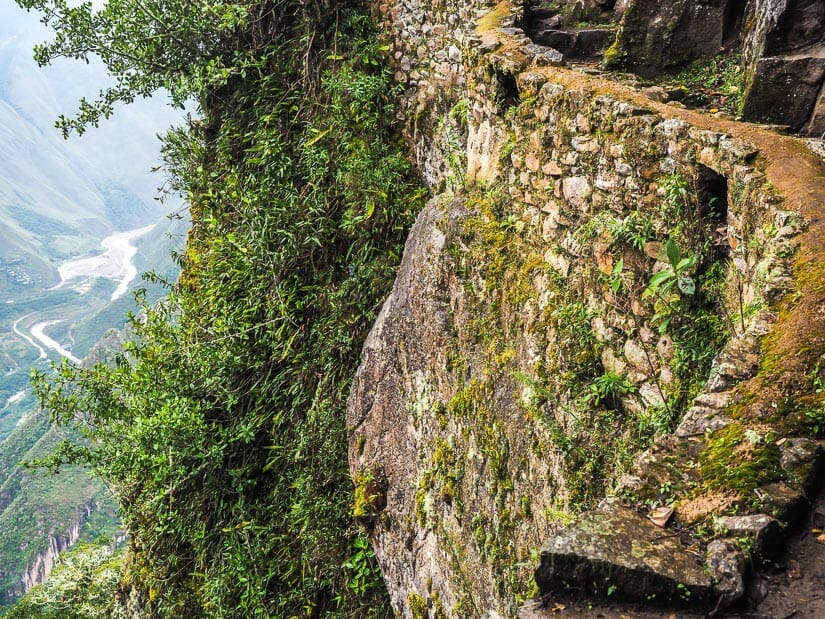 A stone wall supporting a narrow trail along the cliff, with view of river far below to the left