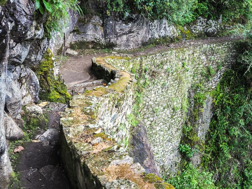 A narrow trail along a stone face, with a steep Inca built stone wall going down the right side