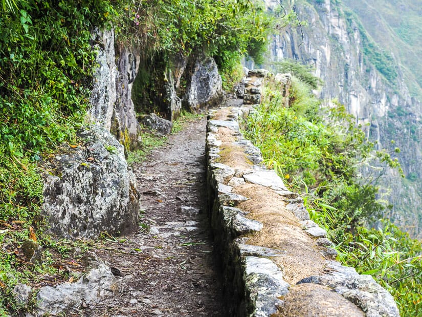 A walking path with rock walls on left and going way down a cliff on the right, with small stone barricade.