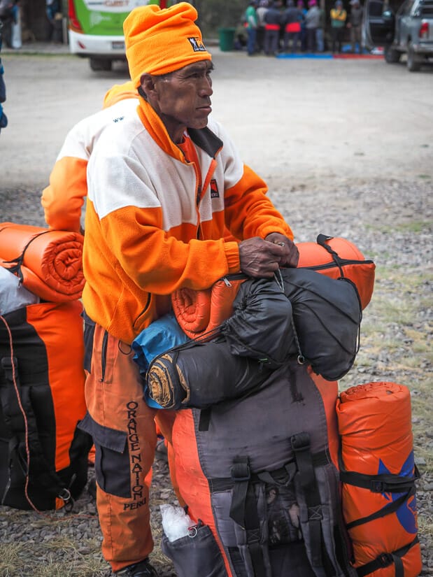 Close up of an Inca Trail porter dressed in orange Sam Travel Peru gear preparing his backpack.