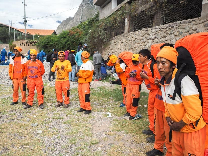 A row of Inca Trail porters all dressed in orange and carrying large packs