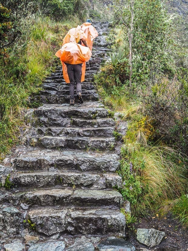 Two trekkers wearing orange ponchos as they ascend a steep staircase on the Inca trail in the rain