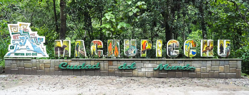A colorful Machu Picchu sign with forest behind it