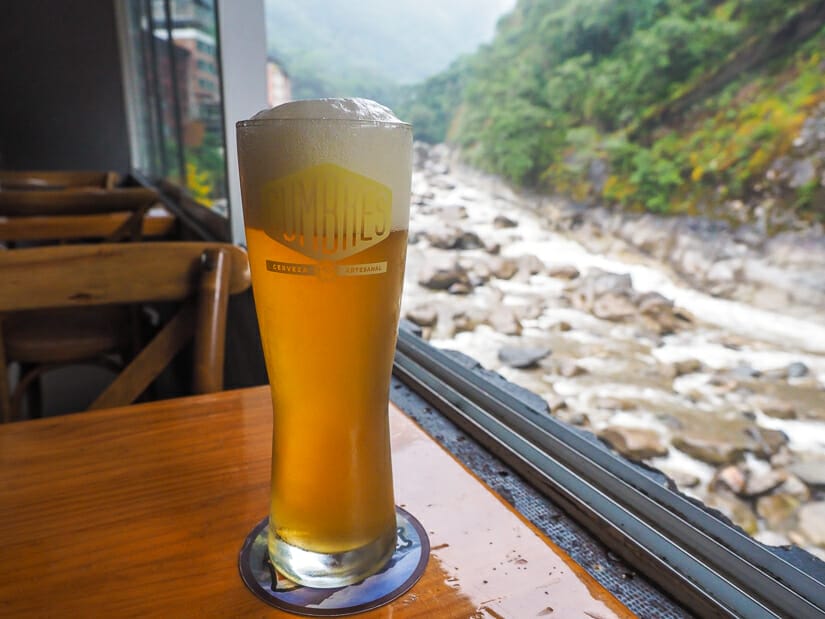 A glass of draft beer on a table at Mapacho restaurant with open window and river flowing behind