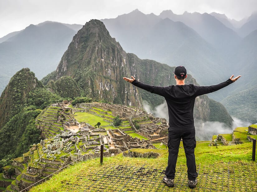 Nick Kembel standing with arms outstretched, facing away from camera, with a view of Machu Picchu