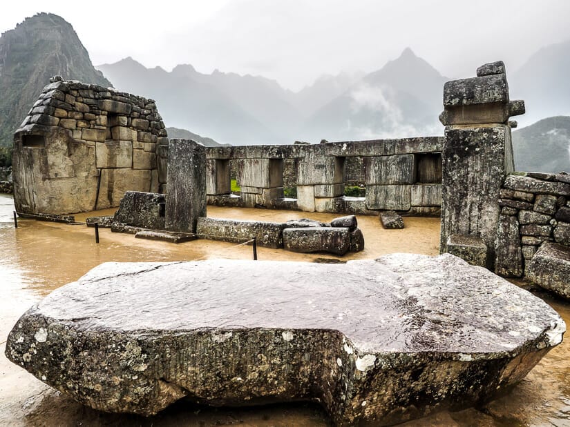 Looking over a large stone toward the Temple of 3 Windows in the Sacred Plaza at Machu PIcchu