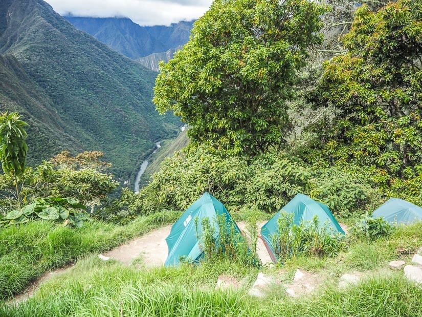 Some green tents on a platform with a view down to a river valley
