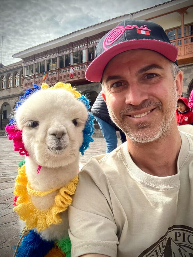 Nick Kembel posing with a baby alpaca wearing colorful accessories in Cusco Peru