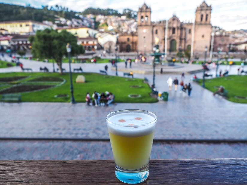 A green pisco sour on a wooden bar overlooking the Plaza de Armas and Cusco Cathedral