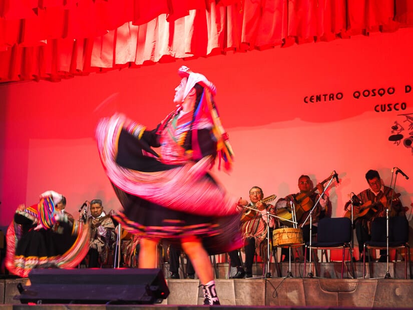 A female Quechua dancer on the stage at Centro Qosqp de Arte Nativo with musicians playing behind her