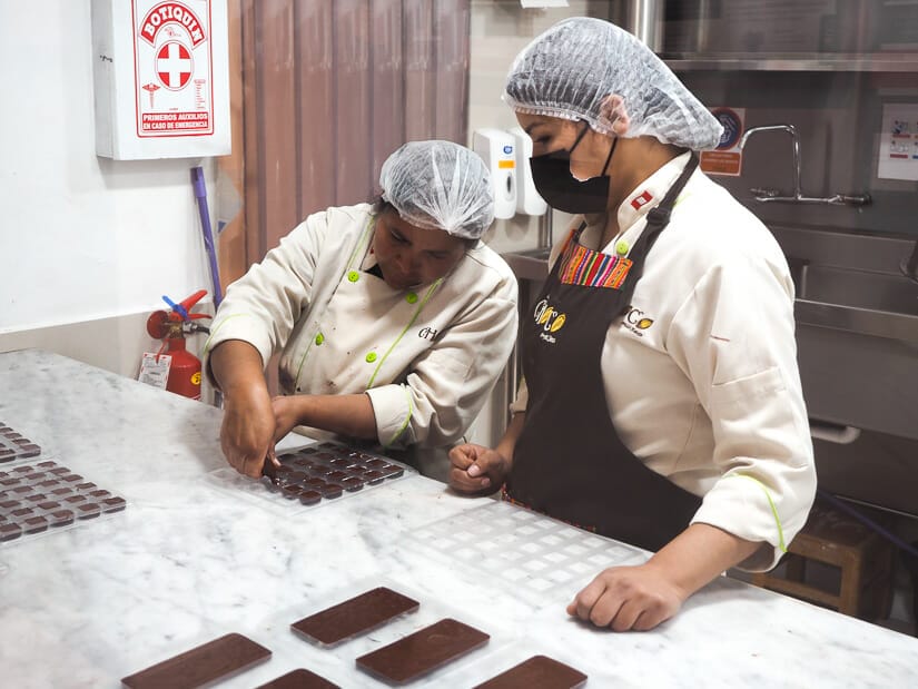 Two women in aprons making chocolates on a counter at ChocMuseo in Cusco