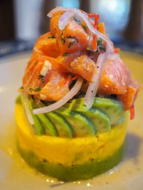 Close up of a dish of yellow causa with avocado and ceviche on top