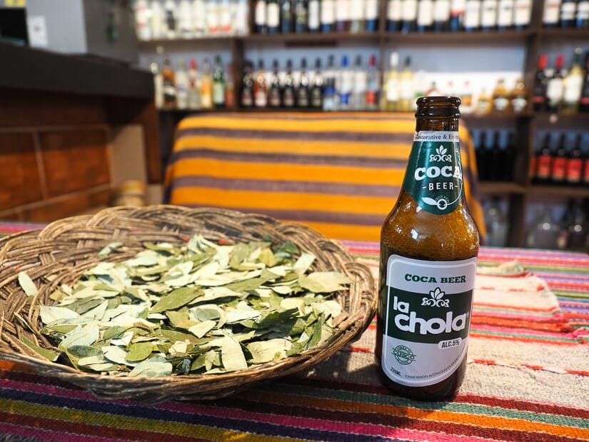 A basket filled with coca leaves and a bottle of coca beer beside it