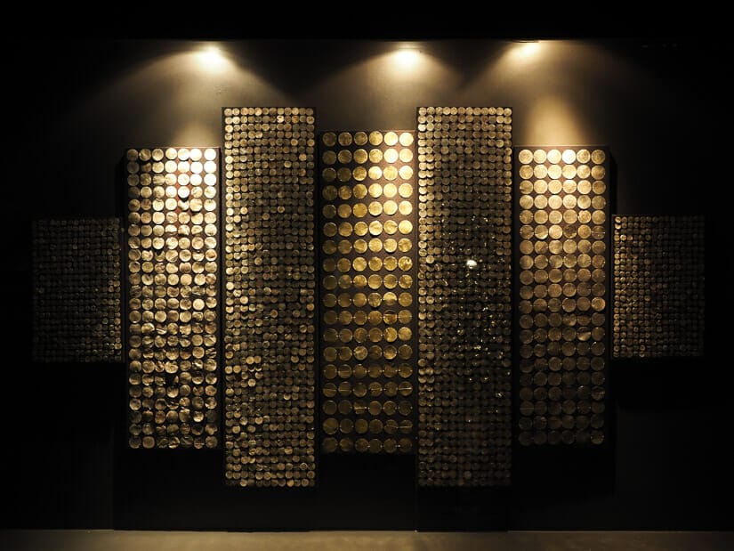 Rows of Inca gold coins displayed on a wall with lights shining on them and black background