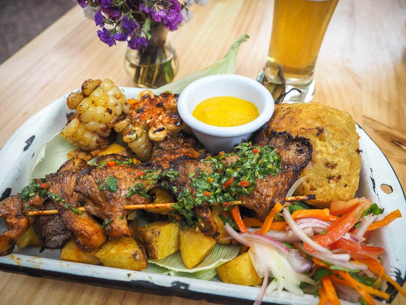 A platter of grilled vegan foods, cheese sauce, plus flowers and glass of beer on the table