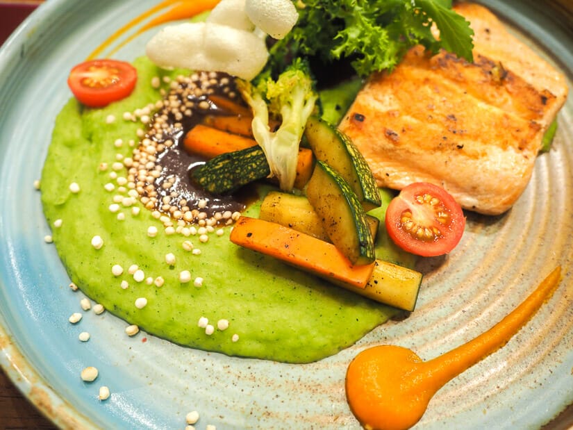 A fancy plate of food with grilled fish, vegetables, and broccoli puree spread across it artistically