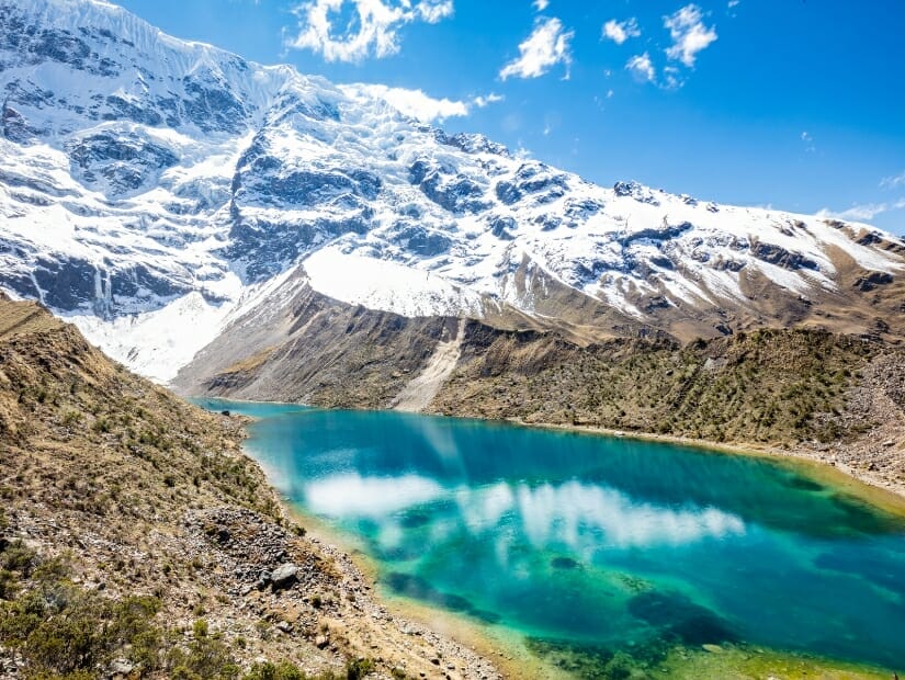 A turquoise colored lake with snow covered mountain behind it