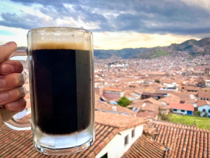 A hand holding up a pint of dark beer with view of Cusco rooftops 