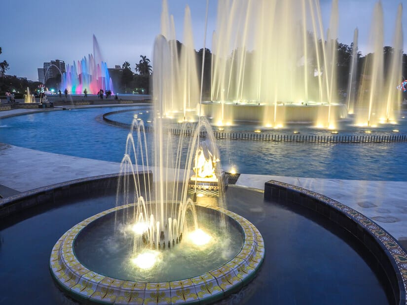 Several water fountains lit up by lights at night