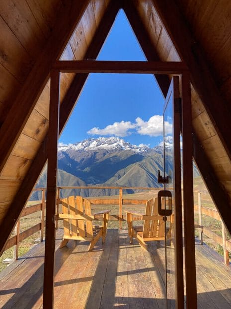 Looking out from an A-frame cabin at mountains, with two chairs on the wooden porch