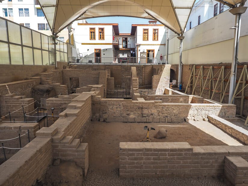 Archaeological site covered by a canopy and building in background