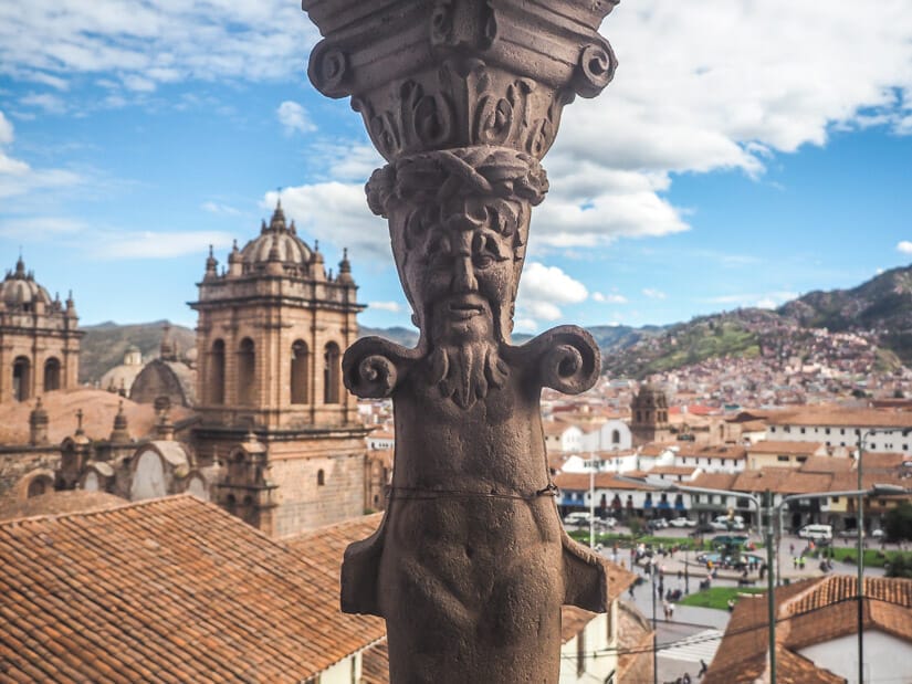 An outer column of a building with a man's bearded face carved onto it, and view of Cusco behind