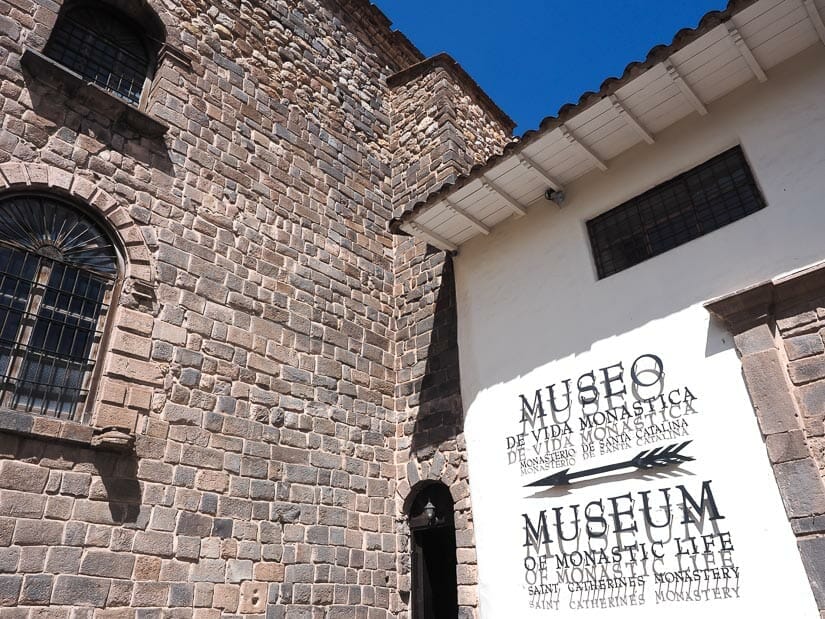 Stone wall meets a white wall, with sign pointing the entrance to the museum of Santa Catalina Monastery